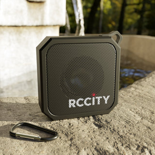 Black portable speaker with 'RCCITY' branding on a stone surface.